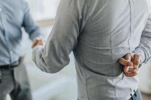 Close up of unrecognizable businessman holding his fingers crossed while shaking hands with his colleague. Concept for Fraudulent Misrepresentation in Business.