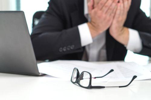 Stressed business man covering face with hands in office. Concept of being served with a lawsuit for breaching a contract.
