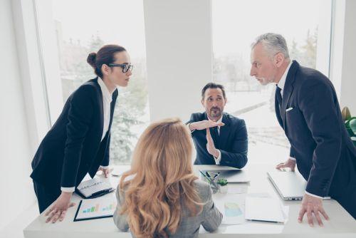 Two stylish business persons in suits having disagreement, war, conflict, standing near desktop in front of each other, face to face with disrespect expression, partner showing stop sign with hands. Concept for business dispute.