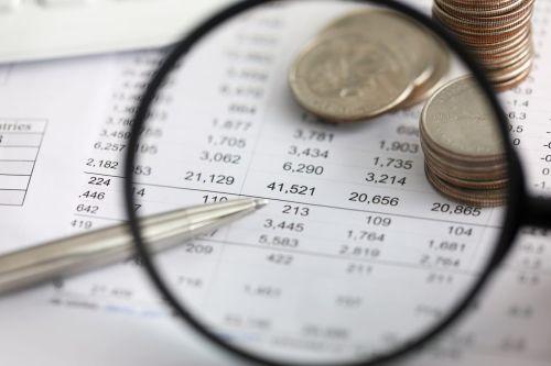 View at financial details in table thru magnifying glass close-up looking for business fraud.