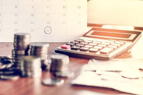 Visual concept for Debt Collection Strategies for Small Businesses blog. Deadline calendar with note, coins,and a calculator on table, background.