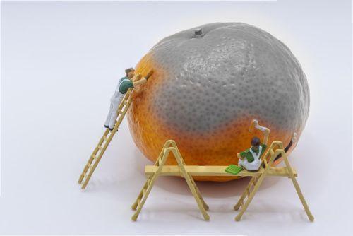 Miniature figures arranged to look like they are painting a tangerine, part of tangerine is grey, the rest orange, painters on ladders and scaffolding as tangerine the size of a house to them. Concept for Deceptive practices