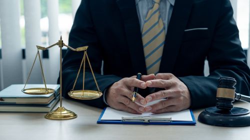 A lawyer or judge works in the office handing the paperwork for a breach of fiduciary duty claim with a hammer and scales of justice on closeup table.